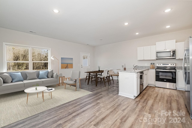 kitchen featuring kitchen peninsula, light wood-type flooring, white cabinetry, light stone countertops, and stainless steel appliances