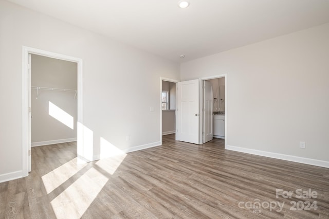 unfurnished bedroom featuring a walk in closet, hardwood / wood-style flooring, ensuite bathroom, and a closet