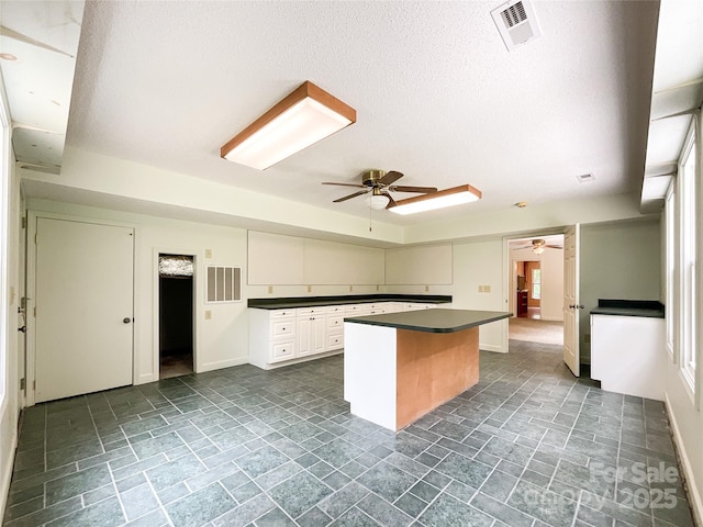 kitchen with ceiling fan, white cabinetry, a textured ceiling, and a kitchen island