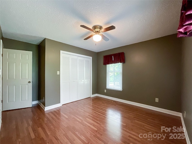 unfurnished bedroom featuring a textured ceiling, a closet, ceiling fan, and hardwood / wood-style flooring