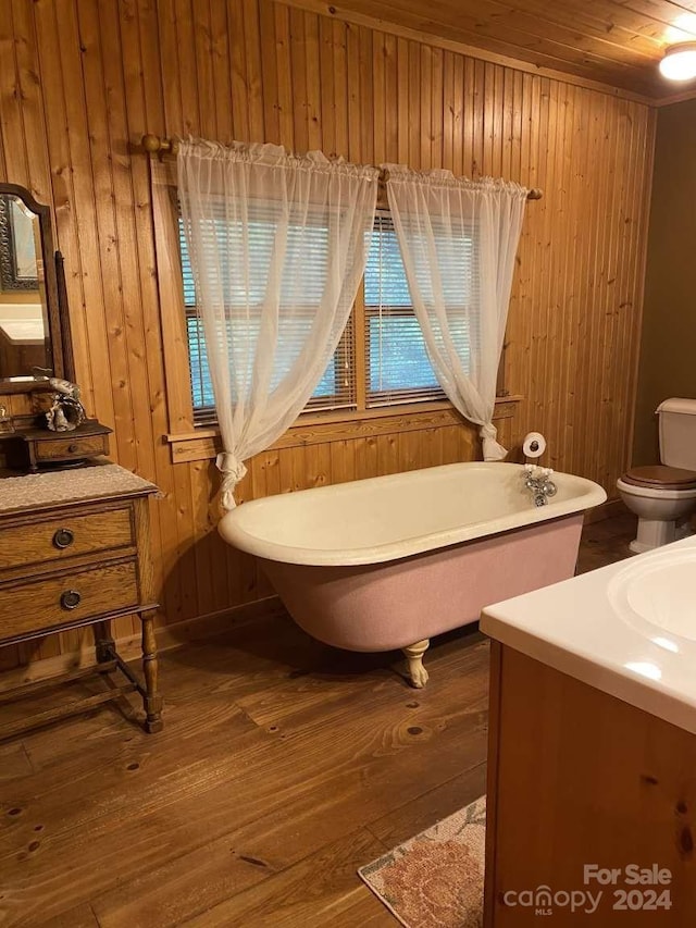 bathroom with a washtub, wood walls, toilet, vanity, and hardwood / wood-style floors