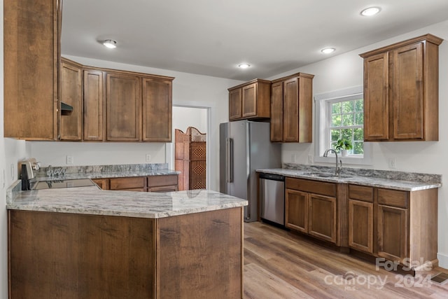 kitchen featuring light stone countertops, stainless steel appliances, light hardwood / wood-style floors, sink, and kitchen peninsula