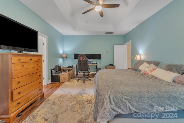 bedroom featuring a raised ceiling, ceiling fan, and wood-type flooring