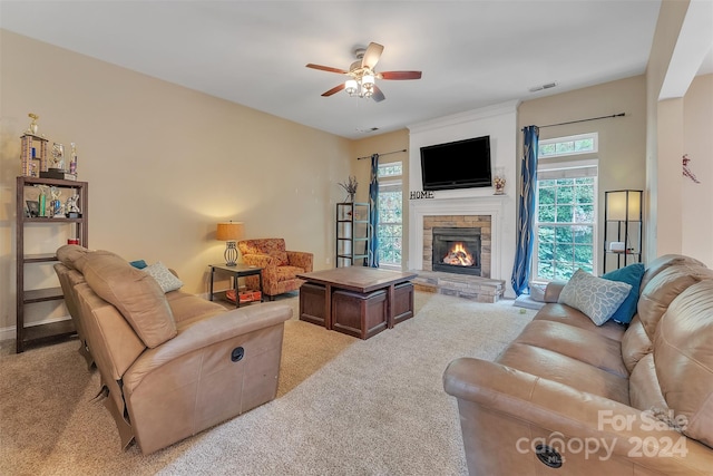 living room featuring a fireplace, light colored carpet, and ceiling fan