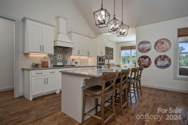 kitchen featuring a center island with sink, a kitchen bar, white cabinetry, dark wood-type flooring, and custom range hood