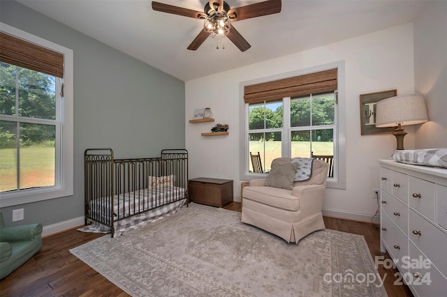 bedroom featuring ceiling fan, a nursery area, multiple windows, and wood-type flooring