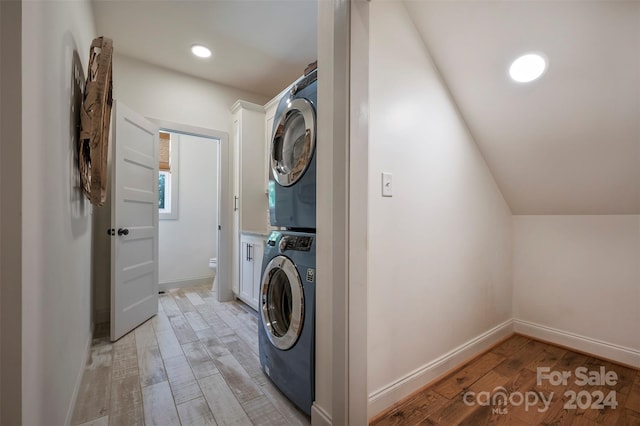 laundry room with stacked washer and clothes dryer, light hardwood / wood-style floors, and cabinets