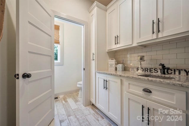 interior space featuring light stone countertops, white cabinets, decorative backsplash, sink, and light wood-type flooring