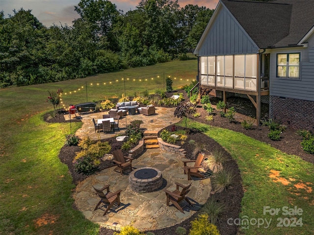 yard at dusk featuring a sunroom, a patio, and an outdoor living space with a fire pit