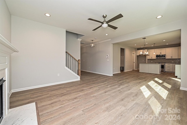 unfurnished living room featuring a fireplace, ceiling fan with notable chandelier, and light hardwood / wood-style flooring