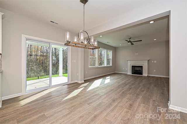 unfurnished living room with a wealth of natural light, wood-type flooring, and ceiling fan with notable chandelier