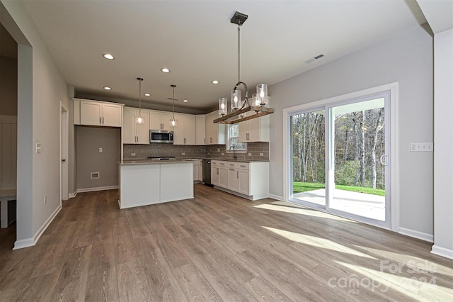 kitchen featuring hanging light fixtures, stainless steel appliances, a kitchen island, light hardwood / wood-style floors, and white cabinets