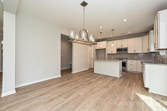 kitchen featuring a center island, sink, hanging light fixtures, stainless steel appliances, and light hardwood / wood-style flooring