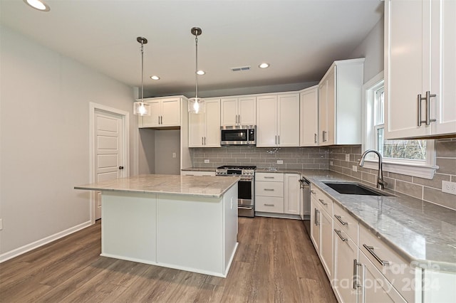 kitchen with appliances with stainless steel finishes, light stone counters, a kitchen island, hardwood / wood-style flooring, and white cabinetry