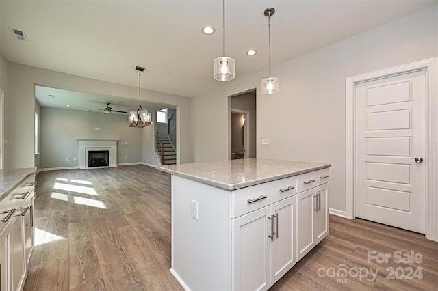 kitchen featuring hanging light fixtures, a kitchen island, light stone countertops, light hardwood / wood-style floors, and white cabinetry