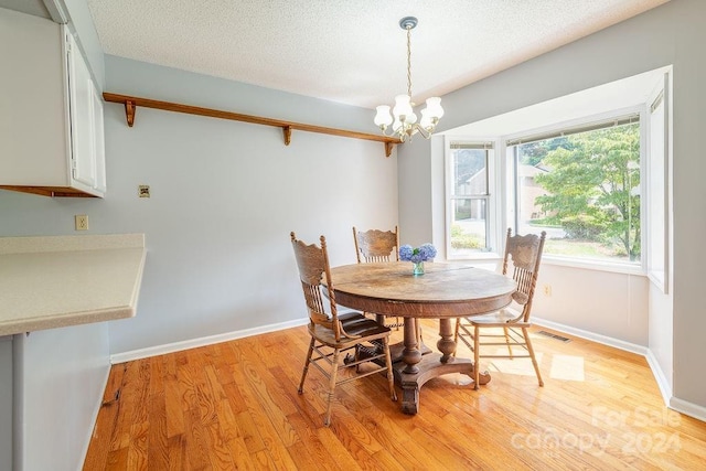 dining room with a textured ceiling, light hardwood / wood-style floors, and an inviting chandelier