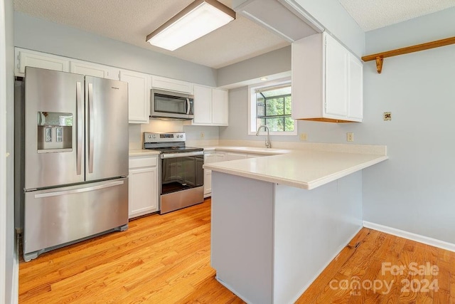 kitchen featuring kitchen peninsula, light wood-type flooring, stainless steel appliances, sink, and white cabinets