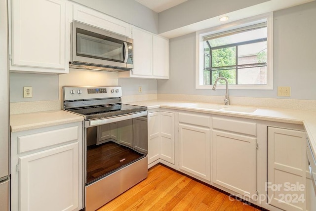 kitchen with appliances with stainless steel finishes, light hardwood / wood-style flooring, white cabinetry, and sink