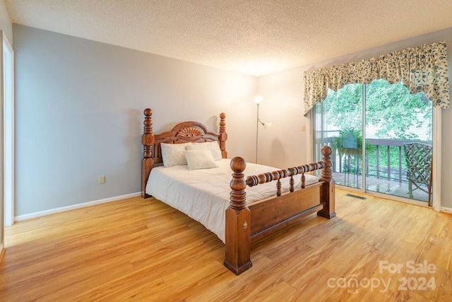 bedroom featuring access to exterior, light hardwood / wood-style floors, and a textured ceiling