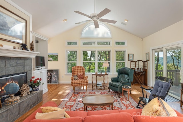 living room featuring a tile fireplace, light hardwood / wood-style floors, vaulted ceiling, and ceiling fan