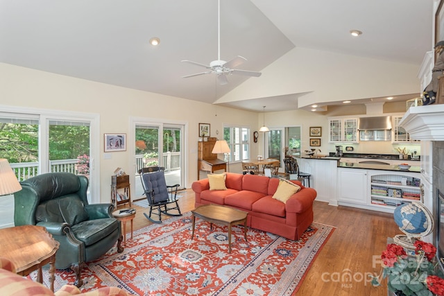 living room with a fireplace, ceiling fan, light hardwood / wood-style flooring, and vaulted ceiling