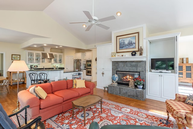 living room with a tile fireplace, ceiling fan, high vaulted ceiling, and light wood-type flooring