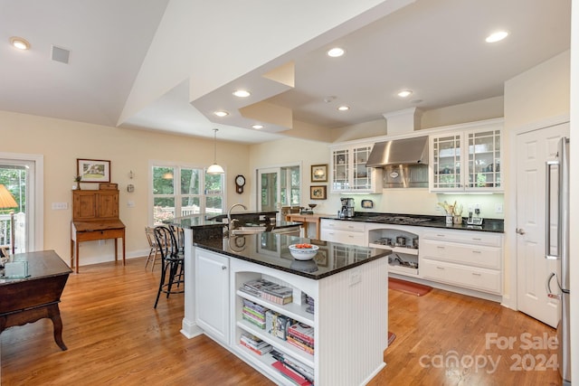 kitchen featuring white cabinets, pendant lighting, a center island with sink, and wall chimney exhaust hood