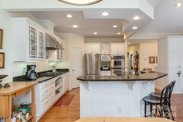 kitchen with light wood-type flooring, a breakfast bar, stainless steel appliances, exhaust hood, and white cabinetry