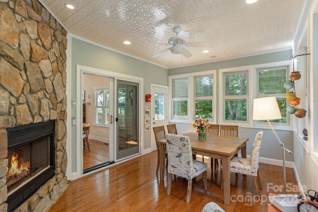 dining room featuring wood-type flooring, a stone fireplace, ceiling fan, and ornamental molding