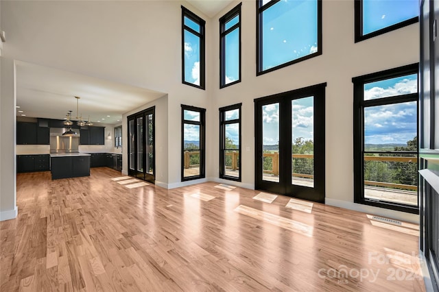 unfurnished living room featuring a high ceiling, a chandelier, and light hardwood / wood-style flooring