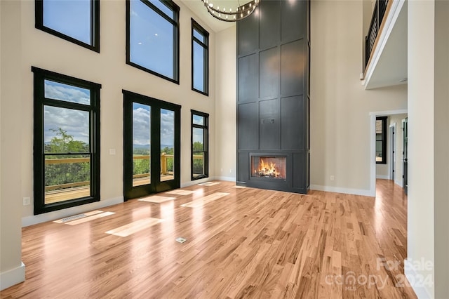 unfurnished living room featuring a towering ceiling, a large fireplace, an inviting chandelier, and light hardwood / wood-style flooring