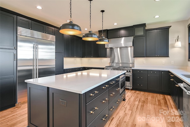 kitchen featuring exhaust hood, a kitchen island, hanging light fixtures, light wood-type flooring, and premium appliances