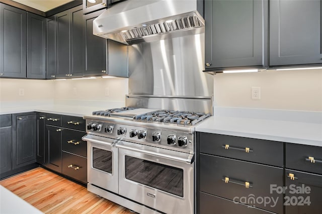 kitchen with wall chimney exhaust hood, light hardwood / wood-style floors, and range with two ovens