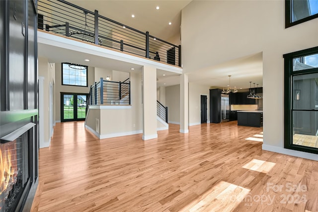 unfurnished living room featuring a high ceiling, a notable chandelier, and light wood-type flooring