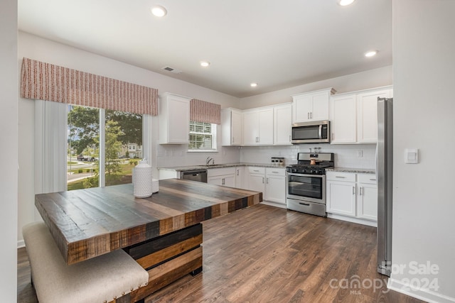 kitchen with appliances with stainless steel finishes, white cabinetry, butcher block counters, tasteful backsplash, and dark hardwood / wood-style floors