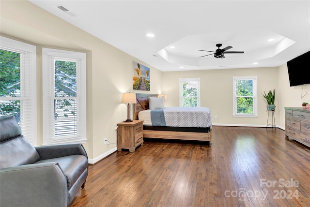 bedroom with ceiling fan, dark wood-type flooring, a tray ceiling, and multiple windows