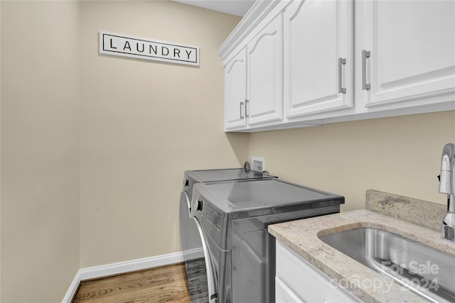 laundry room with washing machine and dryer, cabinets, hardwood / wood-style flooring, and sink