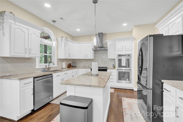 kitchen with wall chimney range hood, a center island, sink, hanging light fixtures, and stainless steel appliances