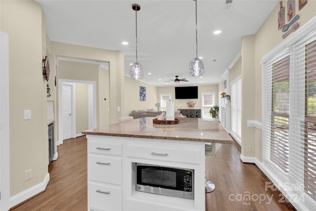 kitchen with white cabinets, hanging light fixtures, stainless steel microwave, and a center island