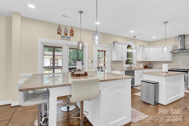 kitchen featuring wall chimney range hood, a kitchen island, decorative backsplash, white cabinetry, and appliances with stainless steel finishes