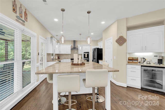 kitchen with white cabinets, beverage cooler, wall chimney exhaust hood, black refrigerator, and hanging light fixtures