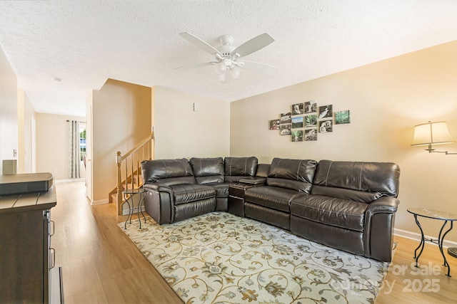 living room with ceiling fan, a textured ceiling, and light wood-type flooring