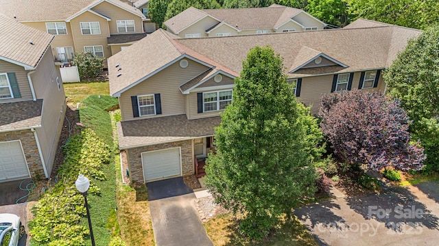 view of front facade featuring a residential view, driveway, stone siding, an attached garage, and a shingled roof
