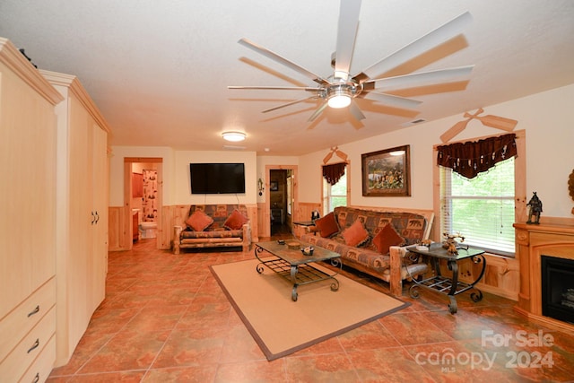 tiled living room featuring a healthy amount of sunlight, ceiling fan, and wooden walls