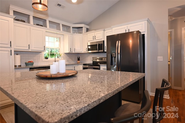 kitchen with light stone counters, white cabinetry, appliances with stainless steel finishes, and vaulted ceiling