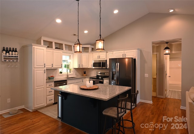 kitchen with white cabinets, appliances with stainless steel finishes, a center island, sink, and light stone counters