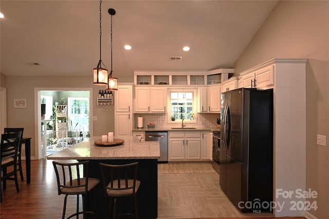 kitchen featuring tasteful backsplash, a kitchen island, stainless steel dishwasher, white cabinetry, and black refrigerator