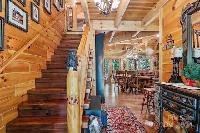 staircase with a notable chandelier, beam ceiling, wood-type flooring, wooden walls, and wood ceiling