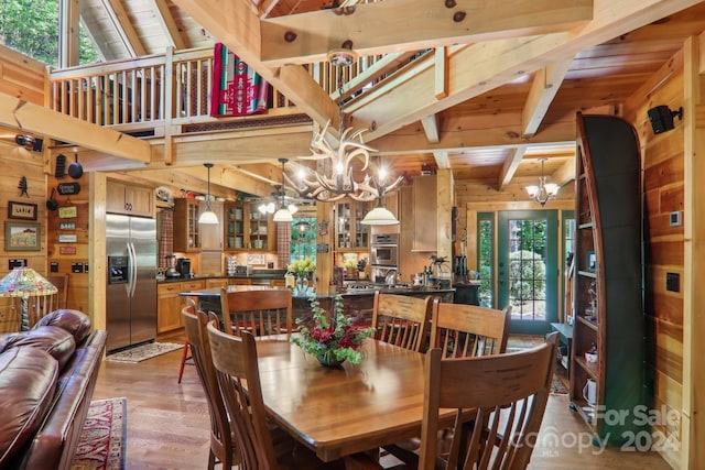 dining space with a healthy amount of sunlight, wood-type flooring, wooden walls, and a notable chandelier