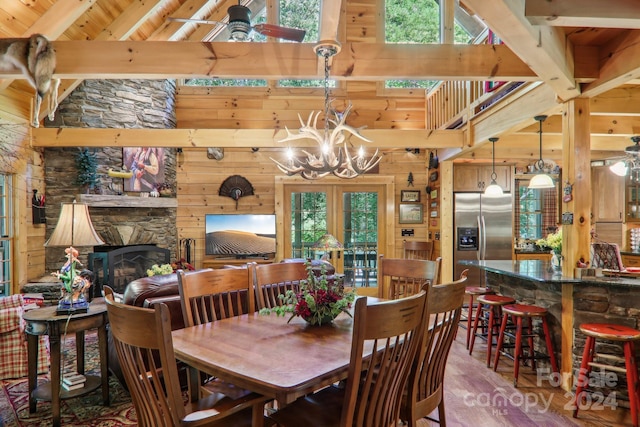 dining room featuring an inviting chandelier, hardwood / wood-style floors, wood walls, a fireplace, and beam ceiling